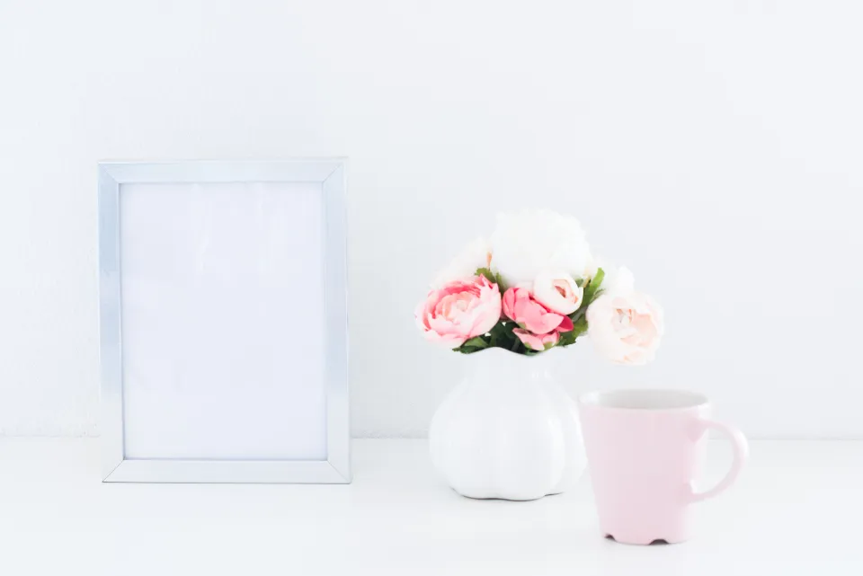 Empty picture frame next to flowers and a mug